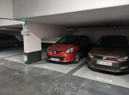 Voiture rouge garée à la place B127 et voiture marron à la B128 dans un parking.