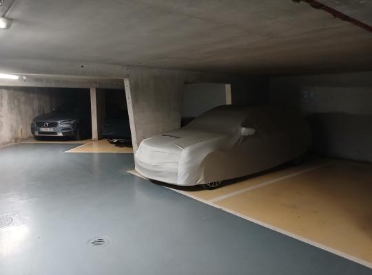 Voiture sous bâche blanche et Volvo grise garées dans un parking souterrain.