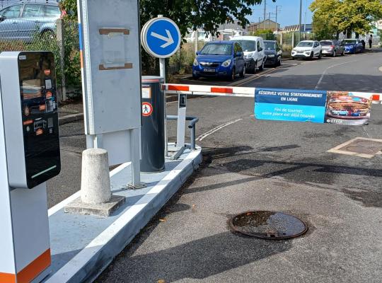 Borne d'accès et barrière automatique à l'entrée du parking extérieur.