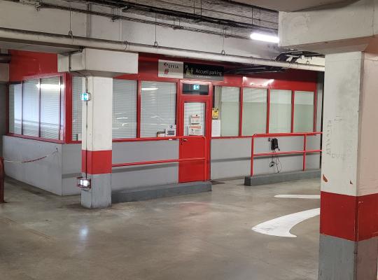 Espace d'accueil du parking vitré aux contours rouges, situé au niveau couvert à proximité de la sortie.