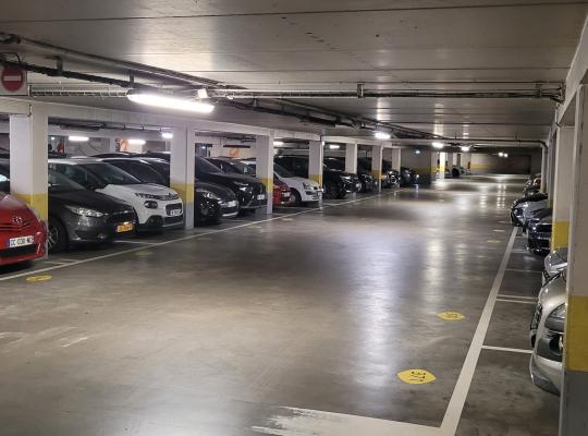 Allée centrale de circulation d'un parking souterrain avec des véhicules stationnés en bataille de chaque côté.