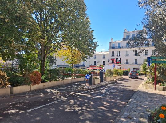 Voie de sortie du parking équipée de barrières automatiques, s'ouvrant sur la rue bordée d'arbres et de bâtiments.