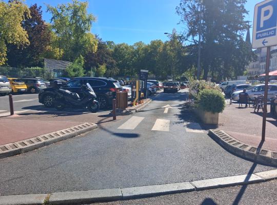 Voie d'accès au parking public matérialisée par un marquage au sol, des bornes de contrôle et un panneau d' signalisation.