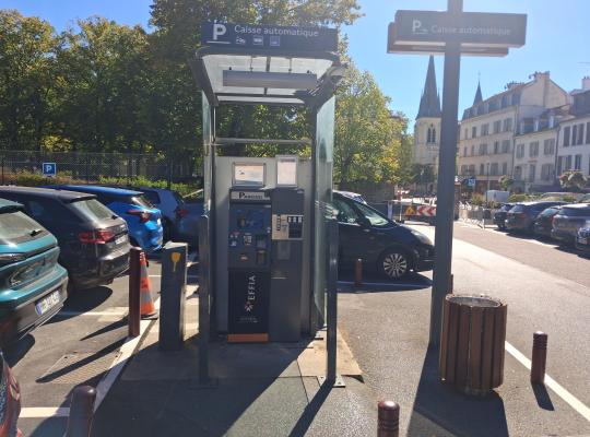 Borne de paiement automatique EFFIA abritée sous une structure vitrée, avec le clocher de l'église en arrière-plan.