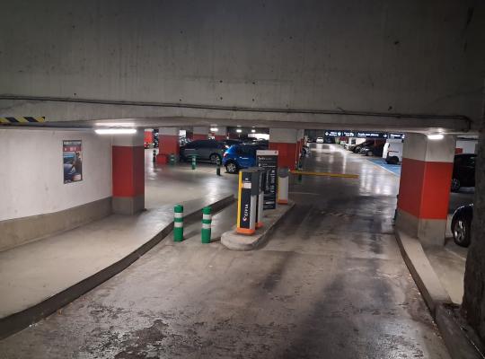 Rampe d'accès intérieure menant à une borne de contrôle et à une barrière automatique dans un parking couvert.