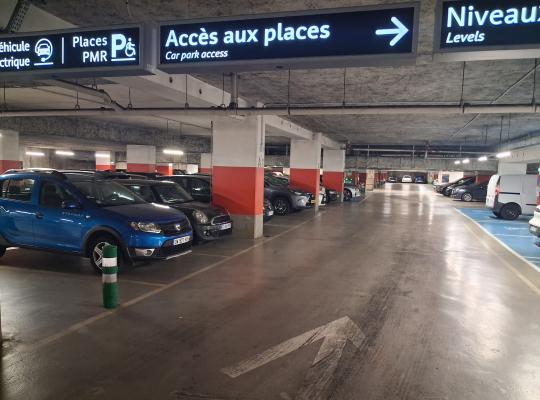 Allée centrale de circulation indiquant l'accès aux places PMR et véhicules électriques avec des voitures garées de chaque côté.