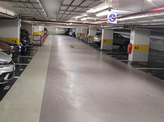 Allée de circulation éclairée desservant des places de stationnement délimitées et numérotées au niveau S3 d'un parking souterrain.