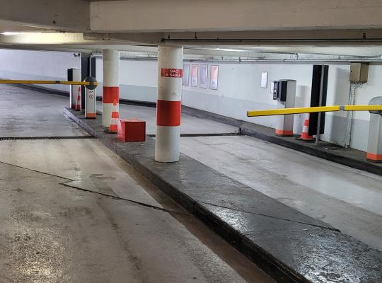 Voies de passage internes à accès réglementé avec barrières levantes jaunes et plots de signalisation dans un parking couvert.