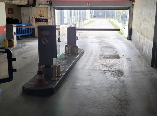 Voie de sortie couverte du parking équipée d'une borne de validation, d'une barrière levante et d'un plot de protection.