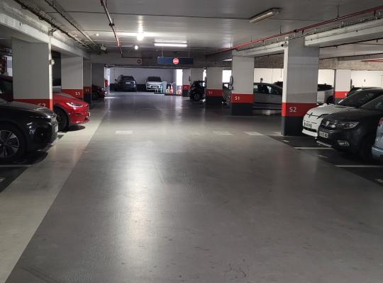 Emplacements de stationnement alignés le long de piliers balisés au niveau S2 d'un parking couvert.