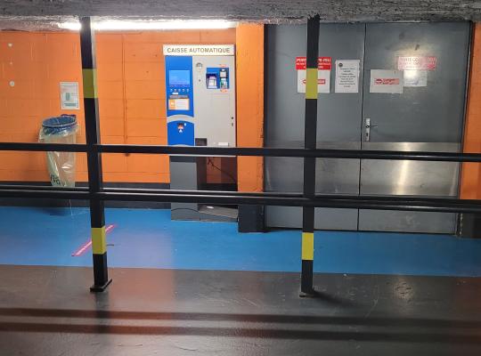 Borne de paiement automatique du parking installée au niveau -1 devant un mur orange vif.