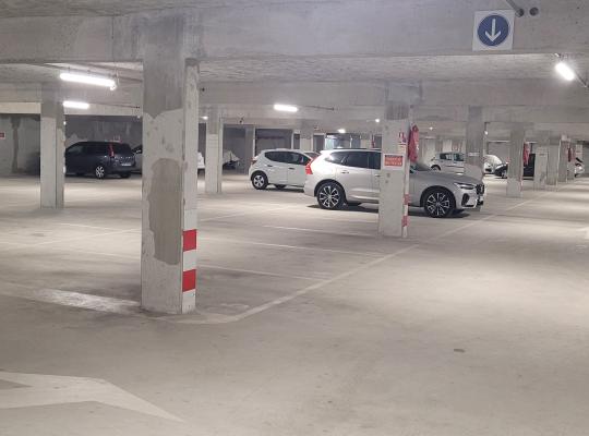 Zone de circulation éclairée desservant des places de stationnement délimitées dans un parking couvert.