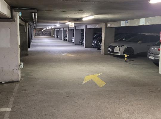 Allée centrale éclairée de circulation dans un parking souterrain desservant des véhicules garés de chaque côté.