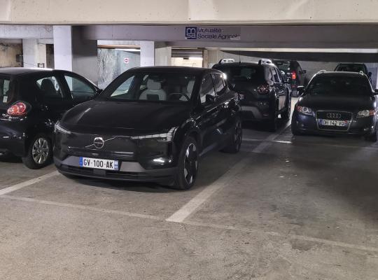 Véhicules stationnés sur des emplacements délimités entre des poteaux de soutien dans un parking couvert.