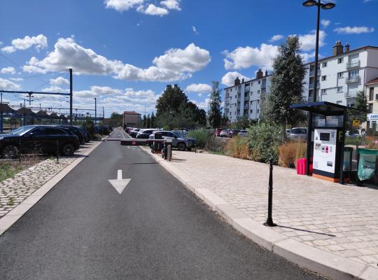 Voie de sortie du parking avec barrière automatique, borne de validation et caisse automatique abritée sur le côté.