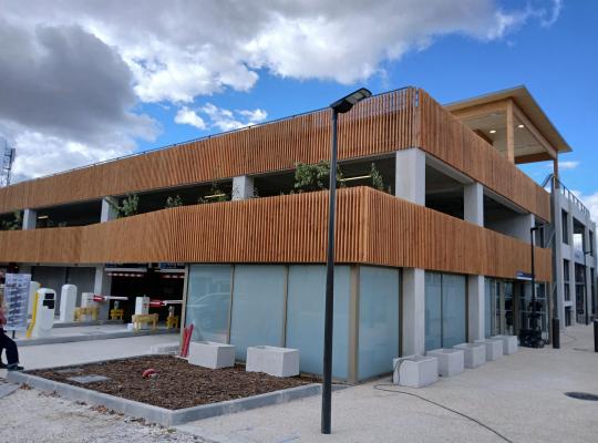 Façade moderne d'un parking silo habillée de bardage bois vertical, avec bornes d'accès au rez-de-chaussée et réverbère au premier plan.