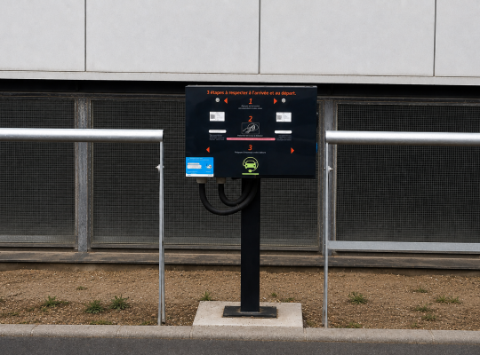 Panneau d'instructions pour la recharge de véhicules électriques fixé près d'un bâtiment moderne.
