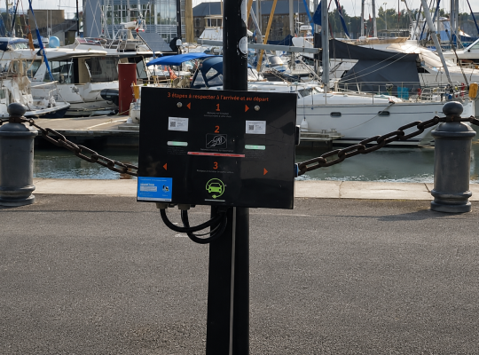 Borne de recharge pour véhicules électriques installée au bord du bassin du port de plaisance.
