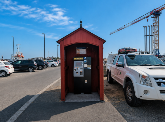 Borne de paiement automatique abritée sous un petit chalet en bois sur le parking.