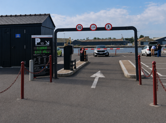 Accès au parking P13 équipé d'un portique de hauteur, de barrières automatiques et d'un panneau d'affichage.