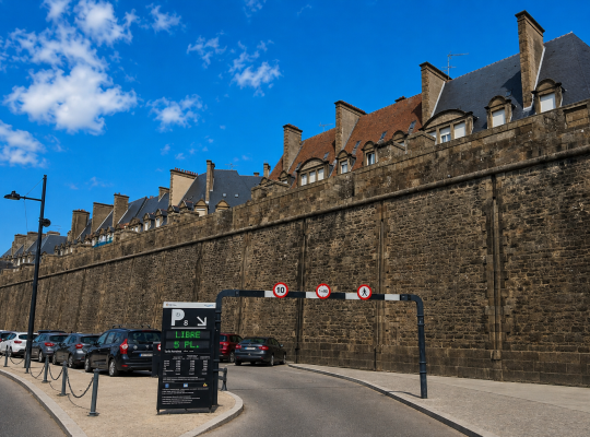 Entrée du parking P8 encadrée par un portique de hauteur et un panneau d'affichage électronique devant la muraille.