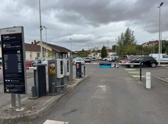 Voie d'accès au parking extérieure équipée de bornes de contrôle à tickets, d'une barrière levante et d'un panneau d'affichage des tarifs.