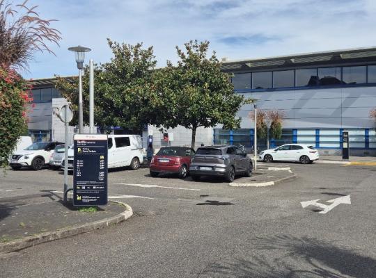 Parking de la gare avec plusieurs véhicules stationnés, panneau d'affichage des tarifs EFFIA et bâtiment ferroviaire en arrière-plan.