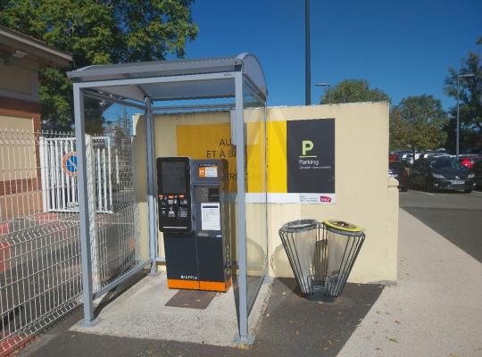 Caisse automatique de paiement EFFIA abritée sous une structure vitrée, installée à côté d'un mur d'information et d'une corbeille de tri.