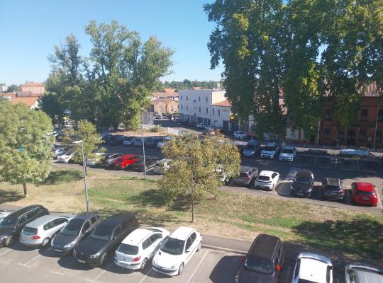 Vue en hauteur d'un grand parking à ciel ouvert bordé d'arbres, avec de nombreux véhicules stationnés.