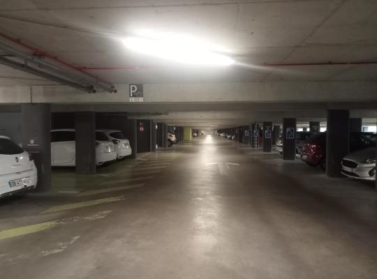 Allée centrale éclairée d'un parking souterrain avec des places de stationnement de chaque côté.