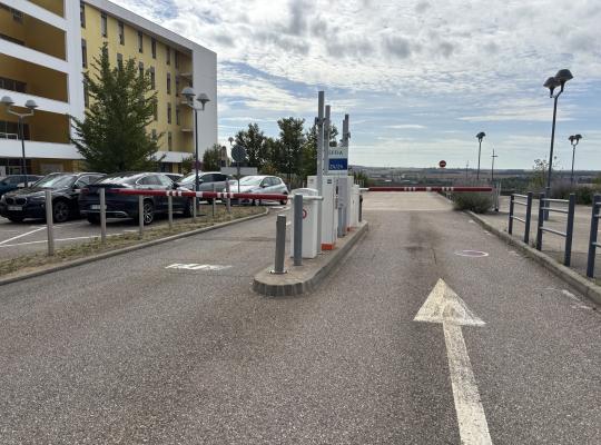 Point de contrôle du parking avec bornes de distribution de tickets et barrières levantes devant les bâtiments hospitaliers.