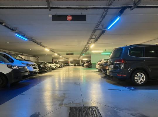 Allée de circulation éclairée desservant des places de stationnement alignées de chaque côté dans un parking couvert.