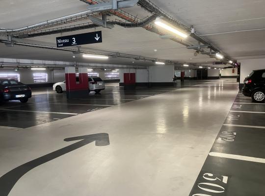 Emplacements de stationnement numérotés au sol au niveau 3 d'un parking couvert, avec signalisation directionnelle.