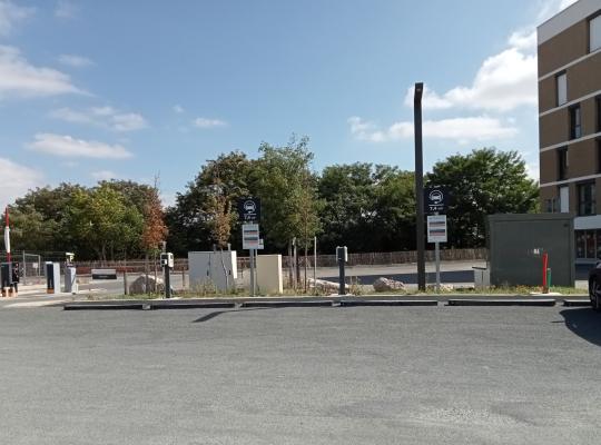 Emplacements de stationnement extérieurs équipés de bornes de recharge pour véhicules électriques avec panneaux d'information.