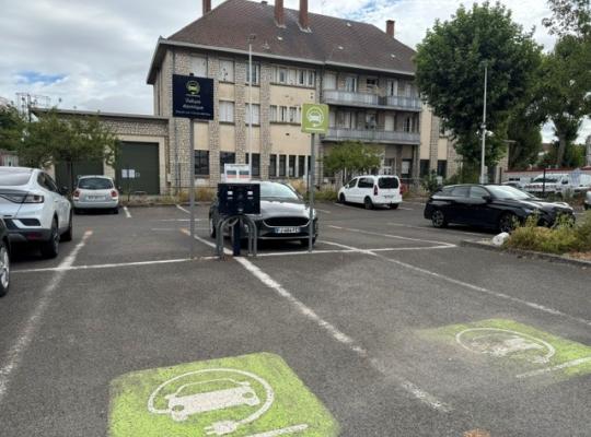 Emplacements de stationnement équipés de bornes de recharge pour véhicules électriques, signalés par un marquage vert au sol.
