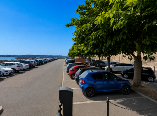 Allée de stationnement arborée longeant les remparts de Saint-Malo et le littoral.