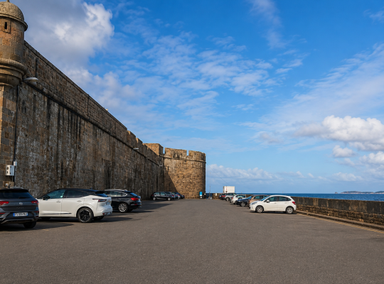Places de stationnement extérieures alignées au pied des remparts historiques et face à la mer.