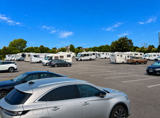 Grande zone de stationnement extérieure accueillant voitures et nombreux camping-cars.