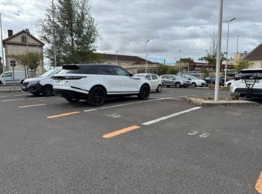 Places de stationnement de surface numérotées au sol, situées sur un parking découvert à proximité des bâtiments.