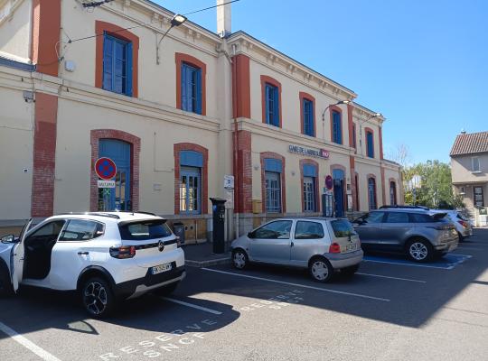 Façade de la gare de L'Arbresle avec places de stationnement réservées SNCF en avant-plan.