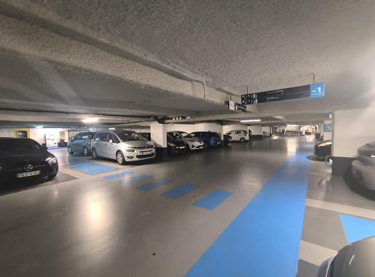 Places de stationnement intérieures au niveau -1, bordées par une bande de circulation bleue et des panneaux d'orientation.