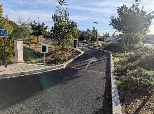 Voie d'accès goudronnée et fléchée menant à l'entrée du parking extérieur.