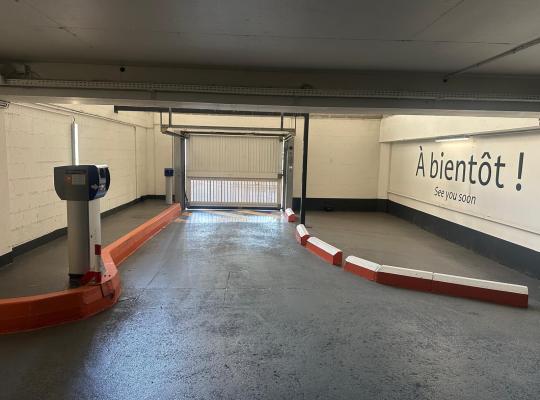 Voie de sortie de parking souterrain avec borne de validation du ticket, portail basculant et inscription « À bientôt ! » sur le mur.