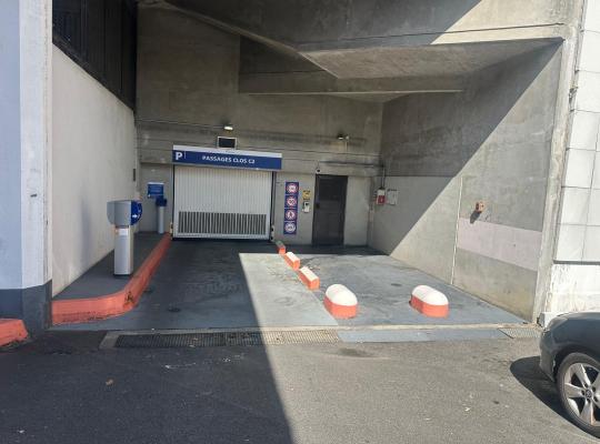 Accès extérieur au parking Passages Clos C2 avec borne de contrôle, porte de garage motorisée et signalétique d'accès.