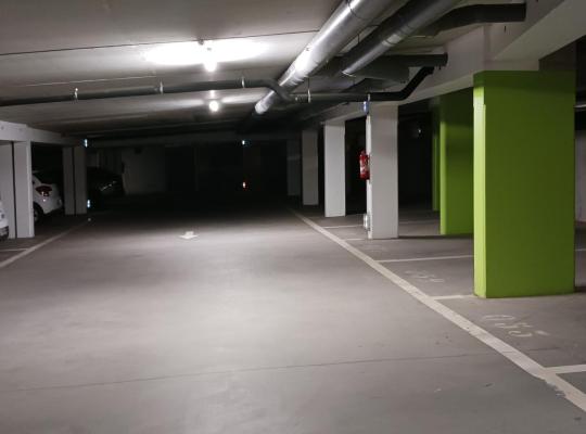 Emplacements de stationnement numérotés dans un parking souterrain éclairé, caractérisé par des piliers peints en vert.