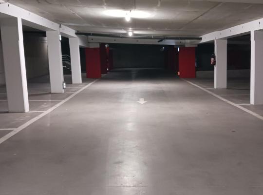 Allée centrale de circulation d'un parking couvert avec fléchage au sol, piliers blancs et poteaux peints en rouge.