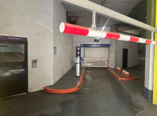 Voie d'accès couverte menant à une porte automatique de parking avec barrière levante et porte piétonne La Boutique.