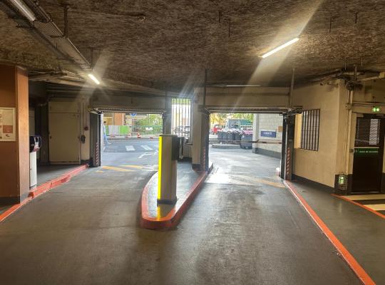 Vue intérieure des voies de sortie du parking couvert avec bornes de validation, portails enroulables et signalétique.