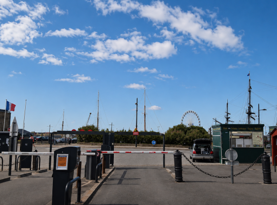 Voie de sortie du parking avec barrière automatique et vue sur les mâtures et la grande roue.