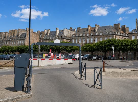 Voie de sortie contrôlée par une barrière automatique face aux bâtiments de la ville intra-muros.